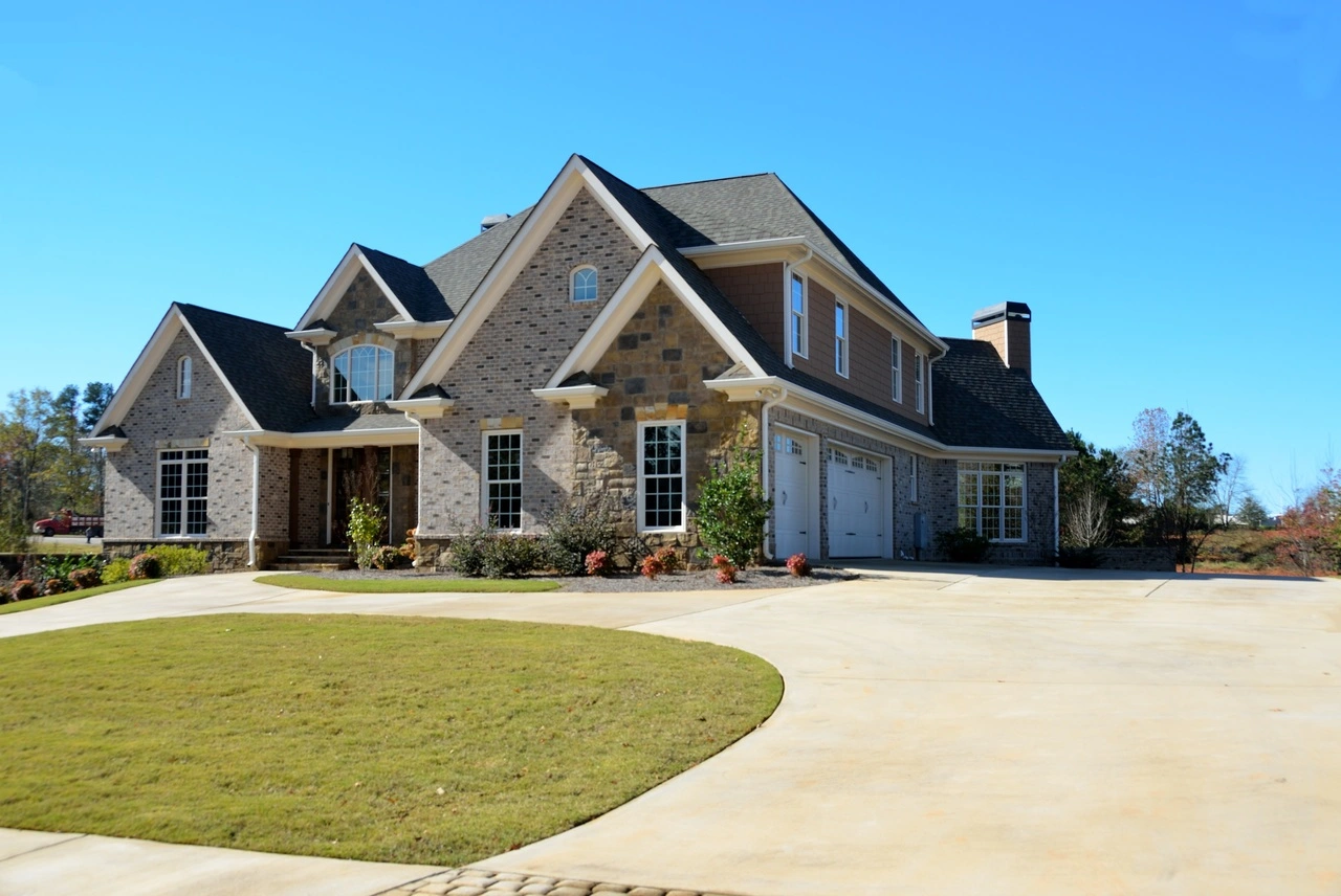 Two-story suburban house with brick and stone exterior, a three-car garage, and a manicured lawn under a clear blue sky.