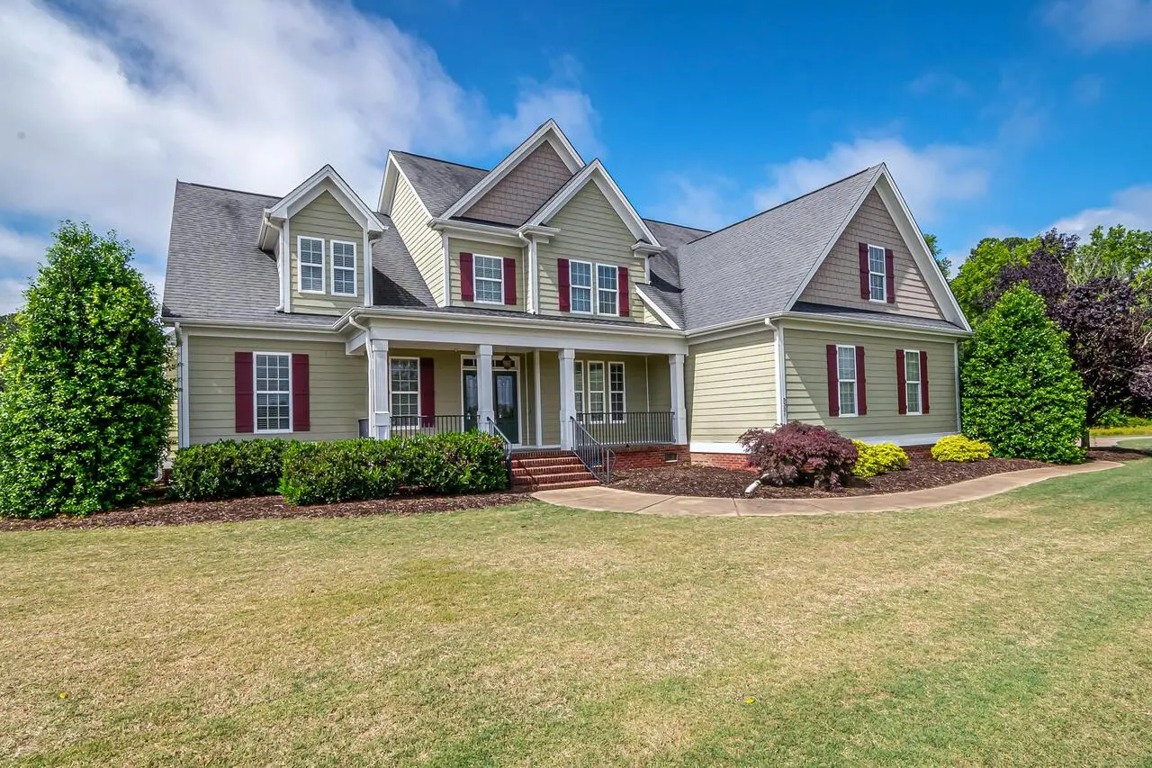 A large two-story house with grey siding, red shutters, and a well-maintained lawn under a bright blue sky.