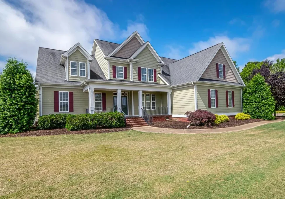 A large two-story house with grey siding, red shutters, and a well-maintained lawn under a bright blue sky.
